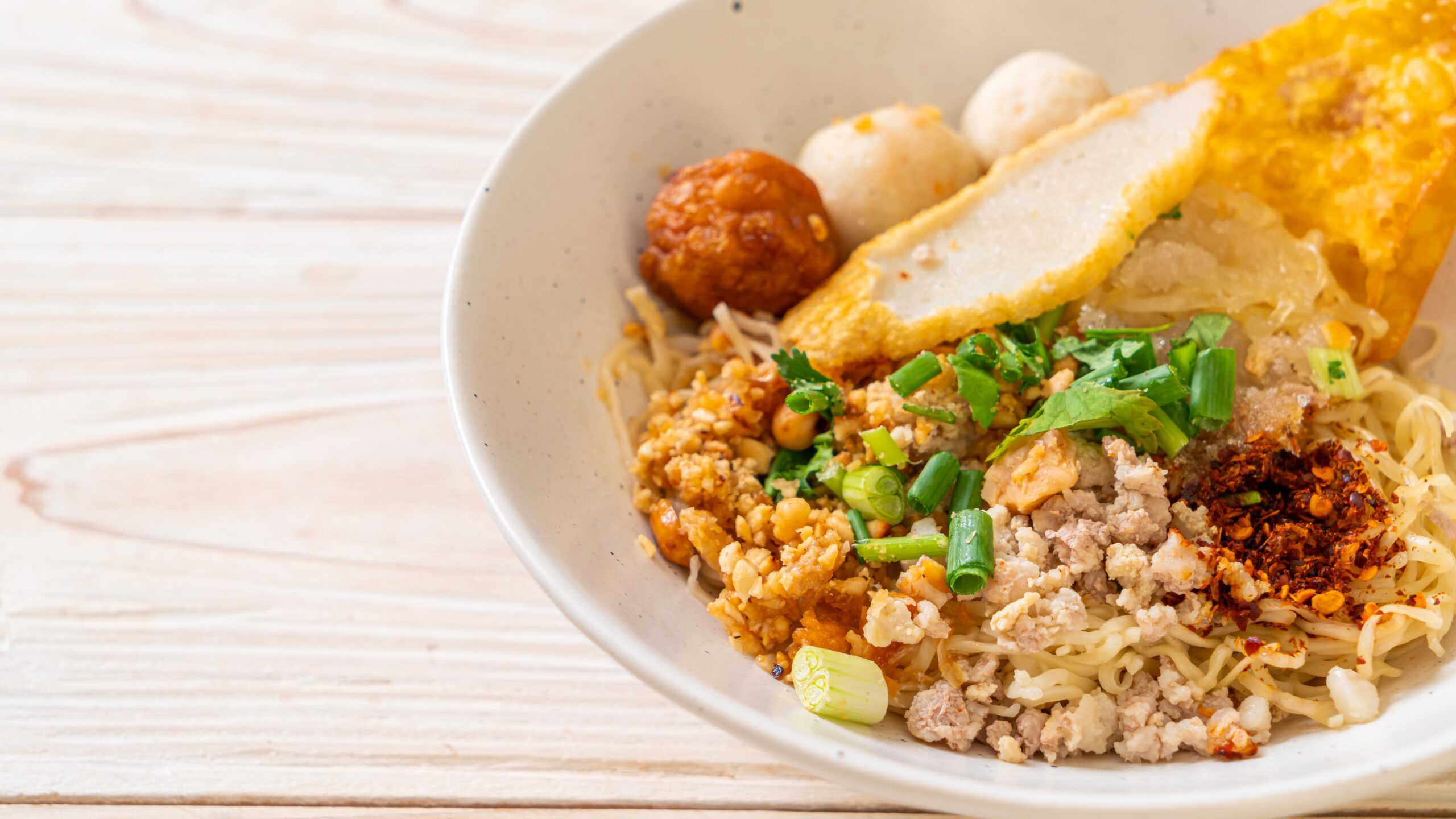 A close-up, high-angle shot of a savory plate of stir-fried noodles served on a circular metal dish. The dark, glossy noodles are tossed with pink shrimp, slices of reddish-brown Chinese sausage, scrambled eggs, fresh green onions, and bean sprouts. Steam rises lightly from the hot dish.