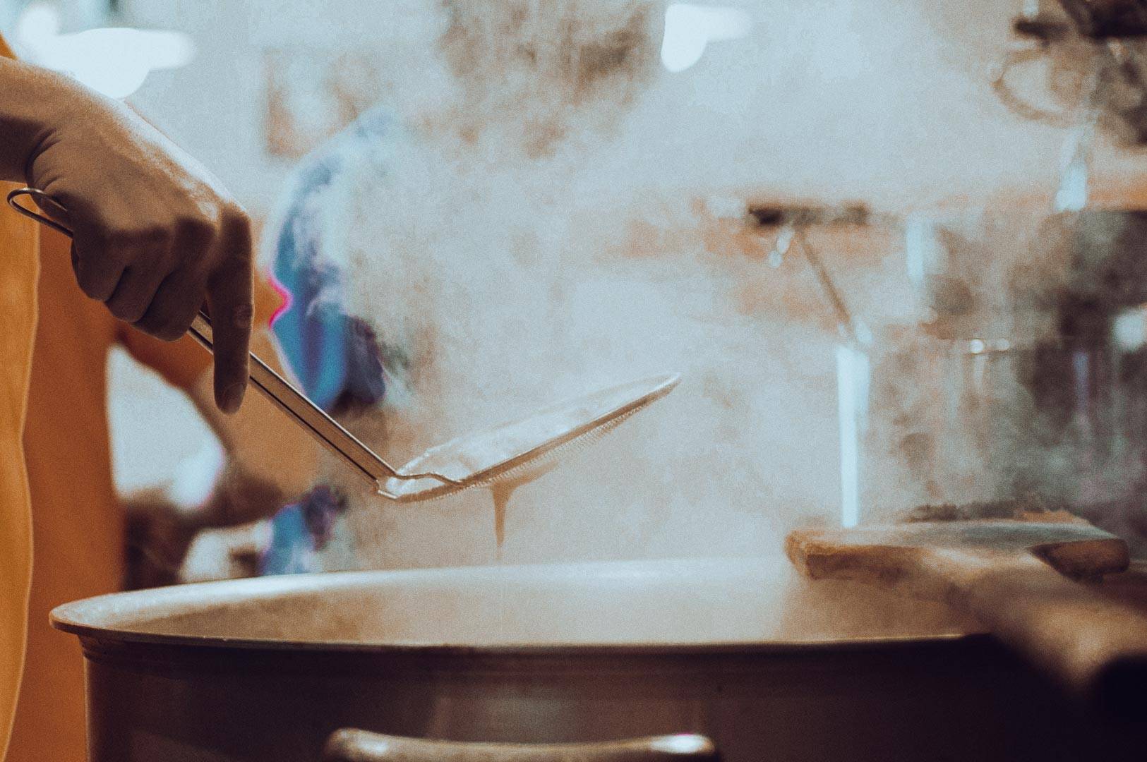 Person stirring a steaming pot in a busy kitchen.