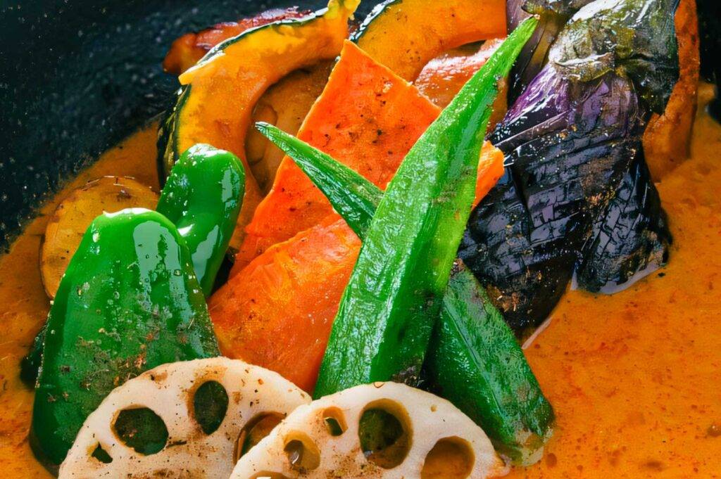 Assorted vegetables such as okra, pumpkin, eggplant, bell pepper, carrot, and lotus root simmered in a creamy orange Hokkaido soup curry base.