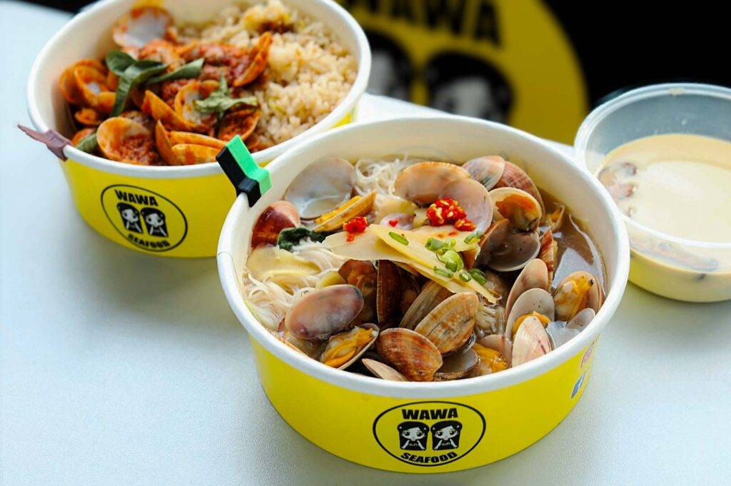 Two takeaway bowls from a seafood restaurant, one filled with clam noodle soup and the other with rice topped with stir‑fried seafood.