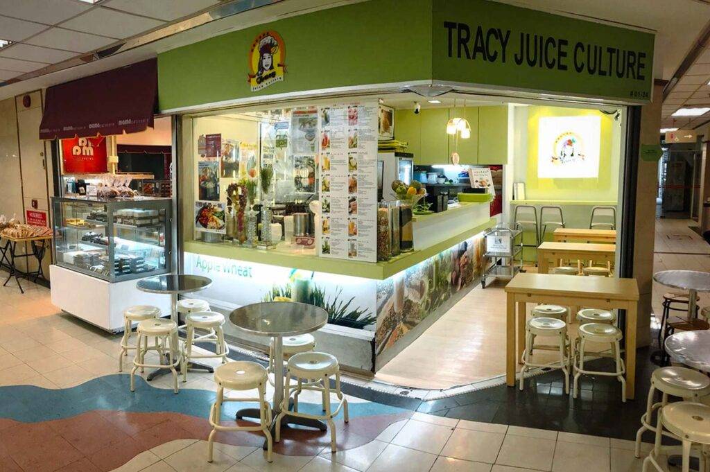 Juice and snack kiosk named Tracy Juice Culture with a counter display, menu boards, and small dining tables in a mall setting.