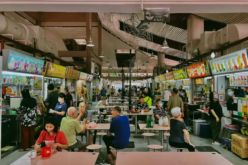 Busy scene inside Changi Village Hawker Centre with diners seated at tables and multiple food stalls operating along both sides of the hall.