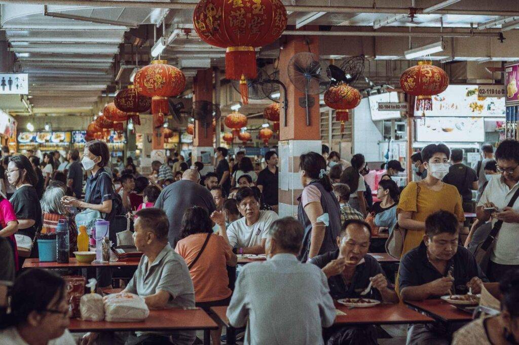 Crowded hawker centre filled with diners and bright red lanterns.