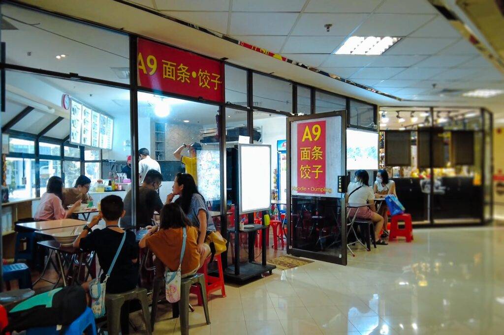 Casual noodle and dumpling shop with indoor seating, customers dining at tables, and a storefront sign displaying Chinese characters.