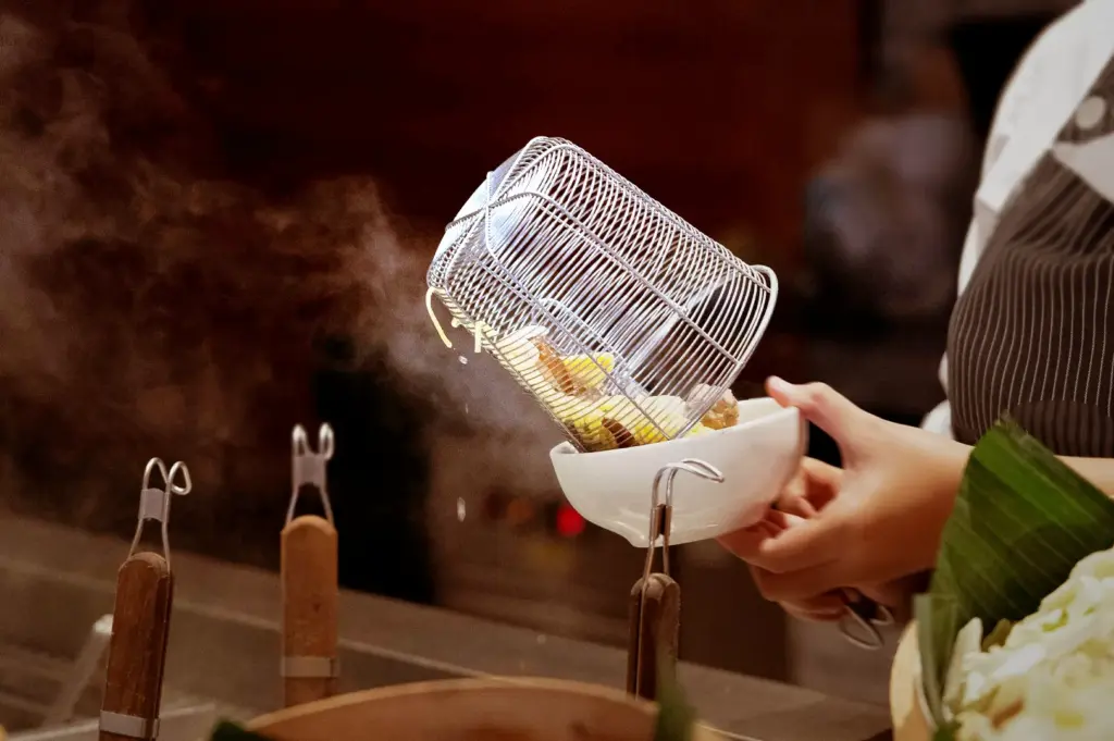 A close-up of preparing noodles for bak chor mee at Teochew Fishball Bak Chor Mee, showing a hawker chef carefully tipping steaming, freshly blanched noodles from a mesh strainer into a bowl, showcasing the precise, hands-on technique involved in crafting this classic Singaporean noodle dish.