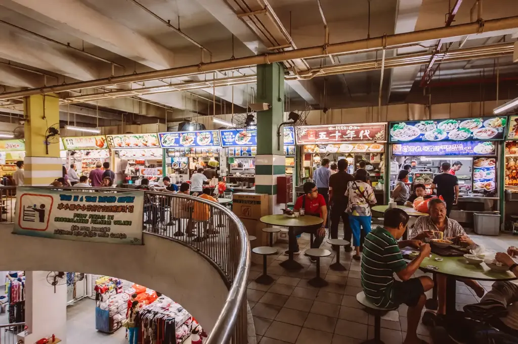 Structured layout of Chinatown Complex Food Centre in Singapore, showing a busy elevated view of organized hawker stall rows, round dining tables, and a curved metal railing overlooking a lower-level market.