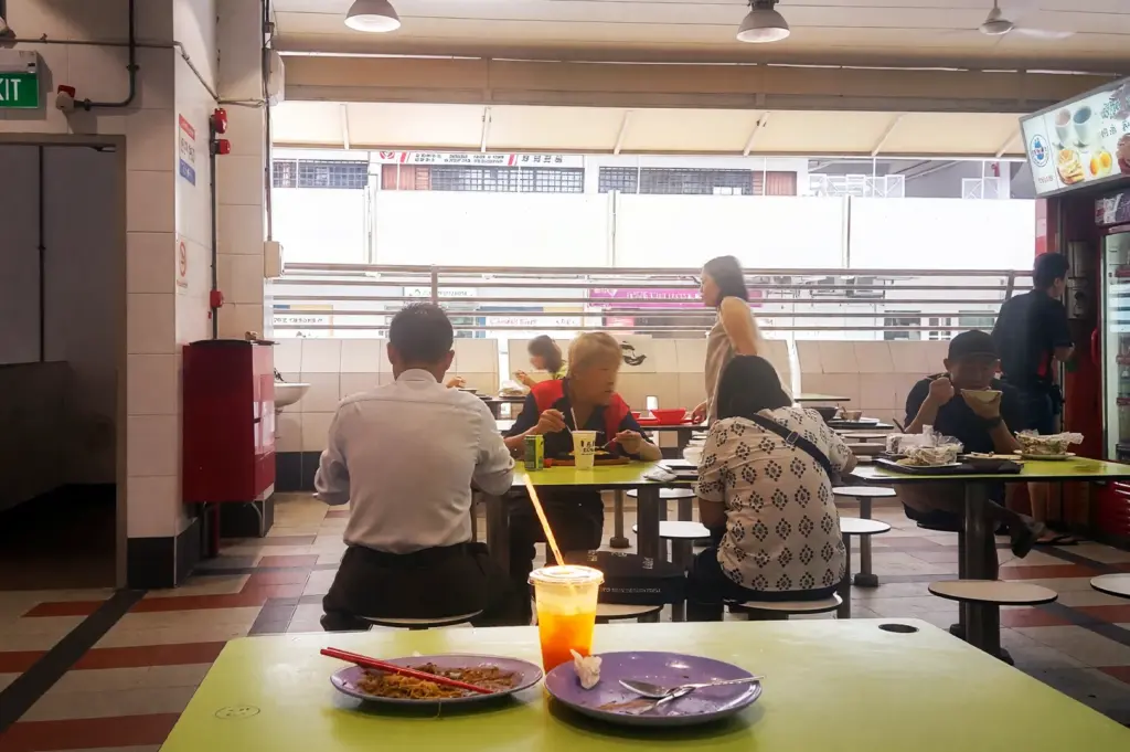 A candid view of the dining area at Tanjong Pagar Plaza Market & Food Centre, featuring patrons enjoying local meals at communal tables, highlighting the bustling, everyday atmosphere of this iconic Singaporean hawker centre.