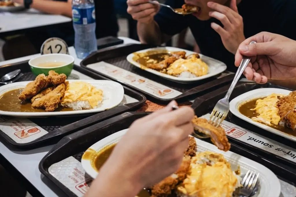 People eating Japanese curry rice with crispy chicken katsu and fluffy omurice eggs on trays at Tanjong Pagar Plaza Market and Food Centre.