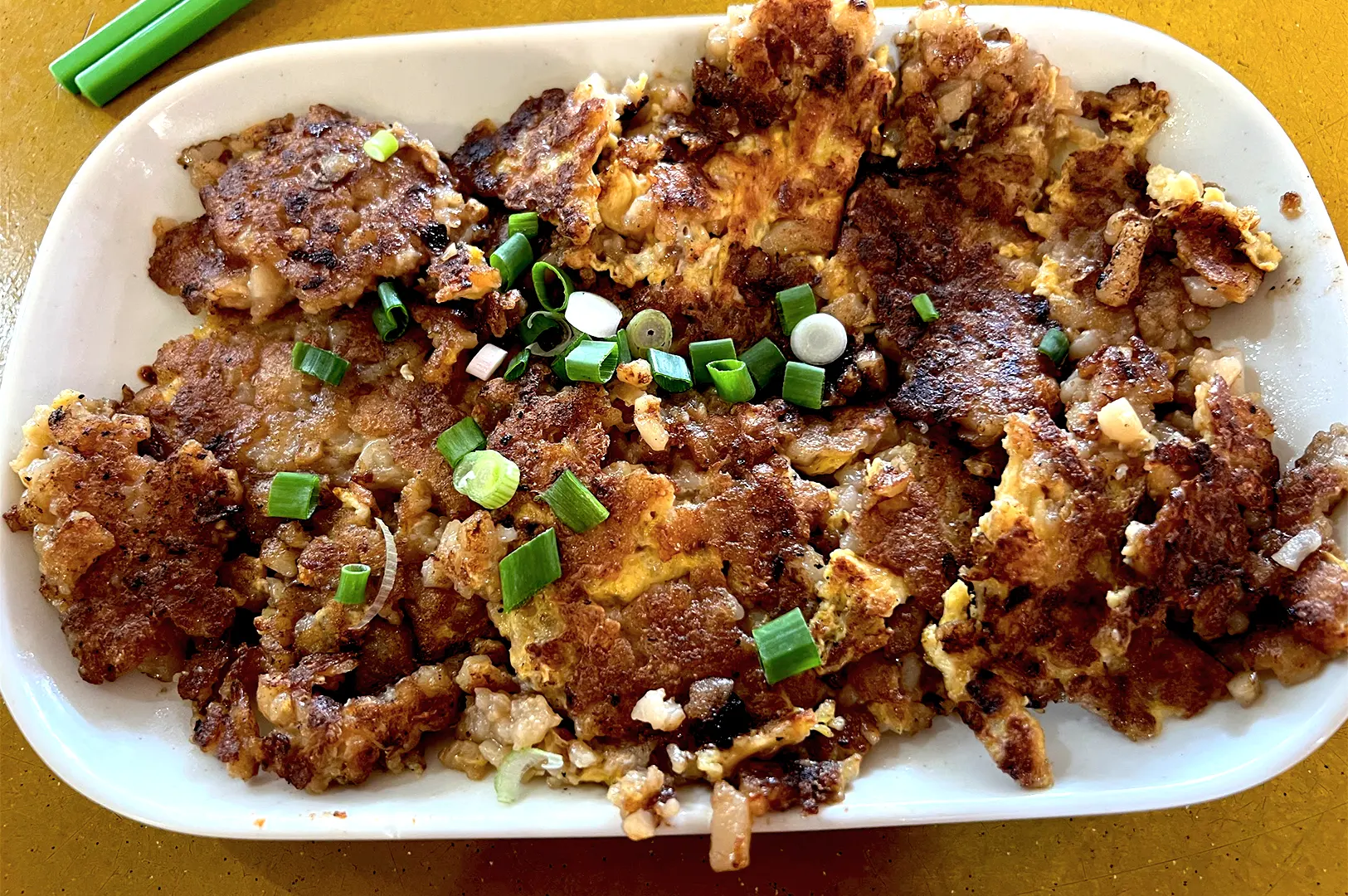 A plate of stir-fried white carrot cake topped with fresh spring onions, served at the iconic Lau Pa Sat hawker centre in Singapore, highlighting the charred, crispy texture of the radish cubes.