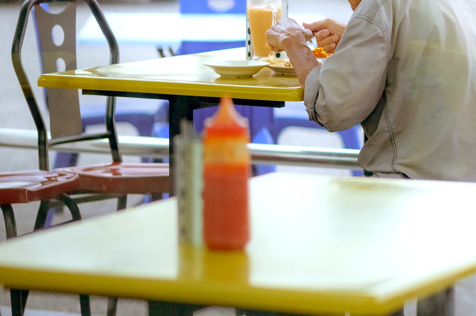 A close-up view of a person eating at a bright yellow table in a Singapore hawker centre, illustrating an editorial study on how seating patterns and behavioral habits reveal routines and social preferences within local food centres.