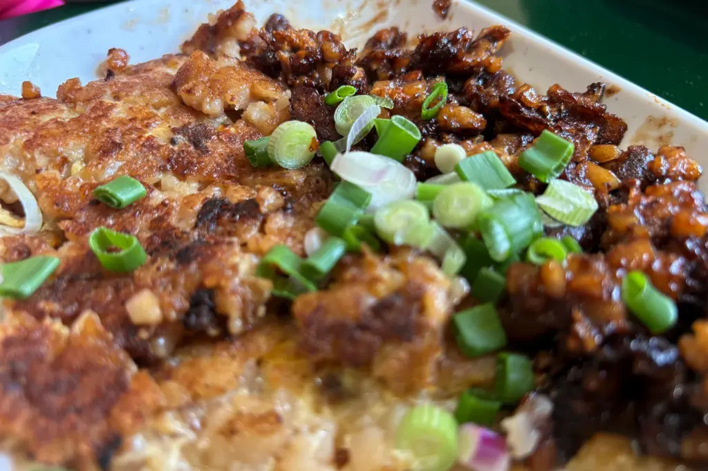 A close-up, high-angle shot focusing on the contrasting textures of savory, dark soy sauce-coated carrot cake and fresh green scallions, capturing the essence of a traditional Singaporean hawker breakfast.