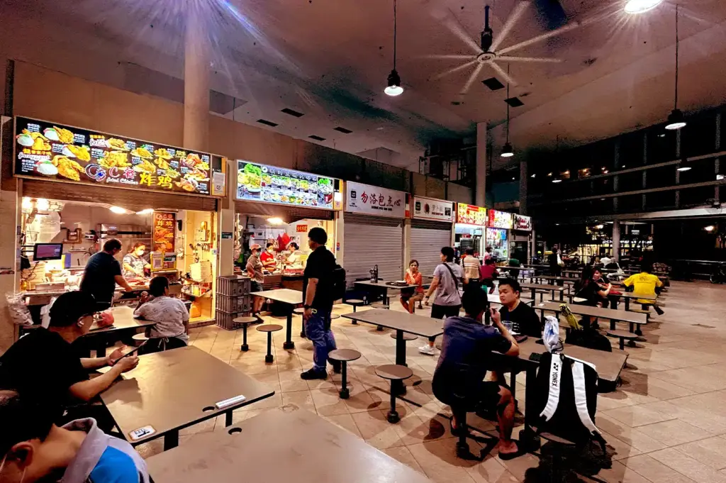 A view of the bustling hawker aisles at Bedok Interchange, featuring rows of diverse food stalls and patrons navigating the busy communal dining space.