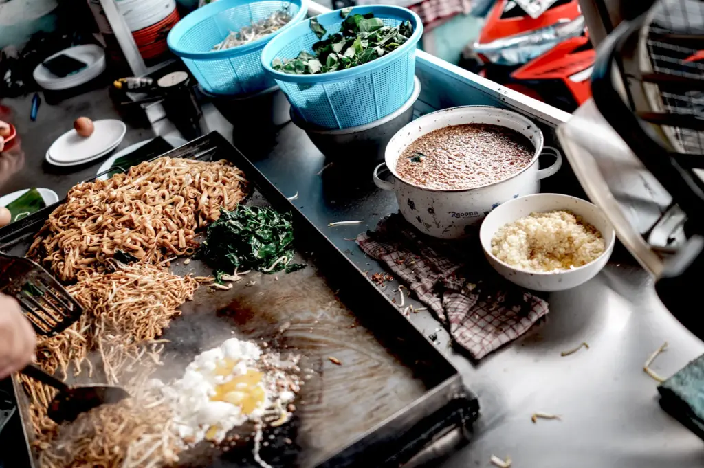 Close-up of a chef cooking char kway teow on a hot flat-top grill at a Fortune Centre stall, highlighting the unhurried preparation of authentic daily meals.
