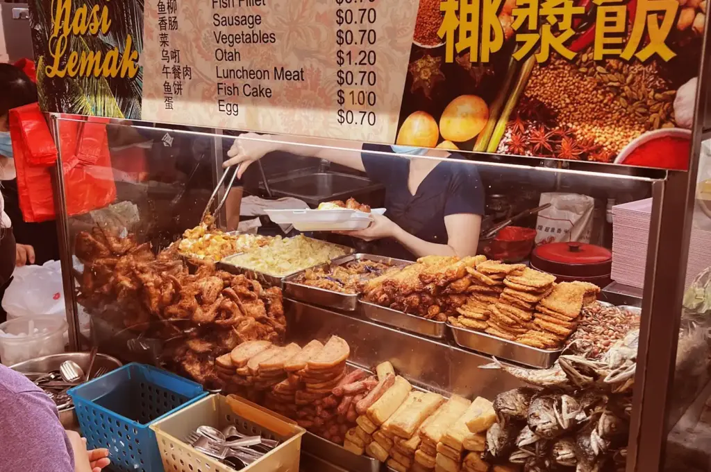A vibrant, well-stocked Nasi Lemak stall display at Bedok Interchange Hawker Centre, highlighting trays of fried chicken, fish cake, and sides, with a clear menu of affordable local delicacies.
