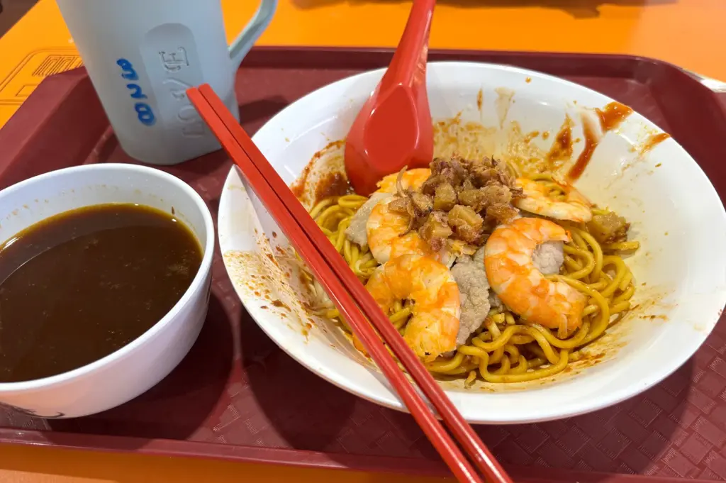 A bowl of prawn noodles resting near the edge of the table