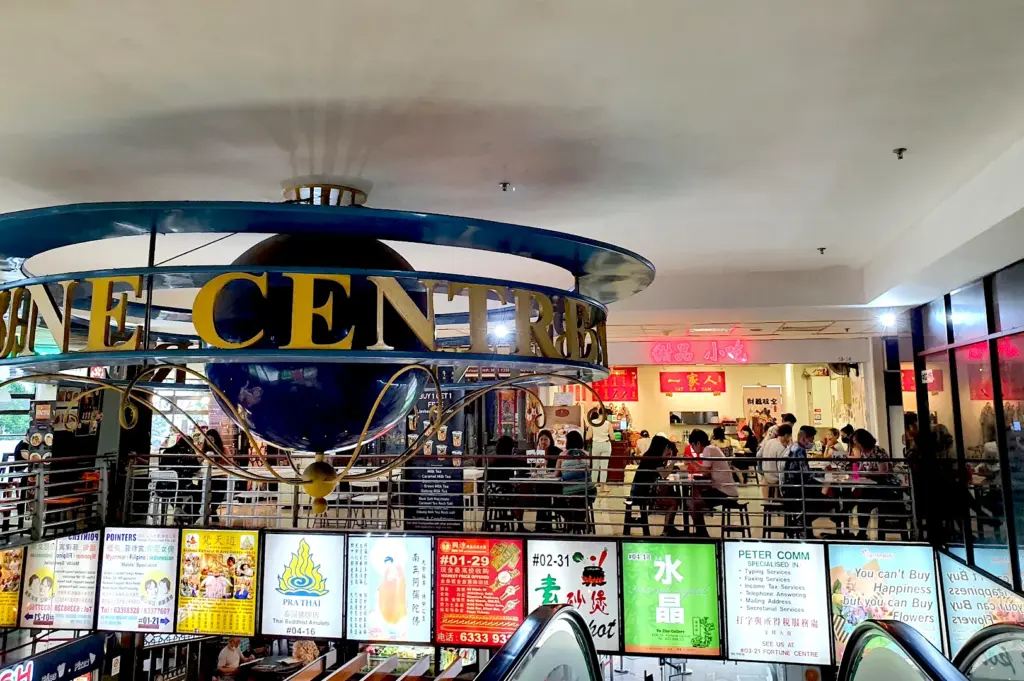 View at Fortune Centre, showcasing its signature globe signage, colorful shopfronts, and the lively community gathering at the center's regular dining tables.
