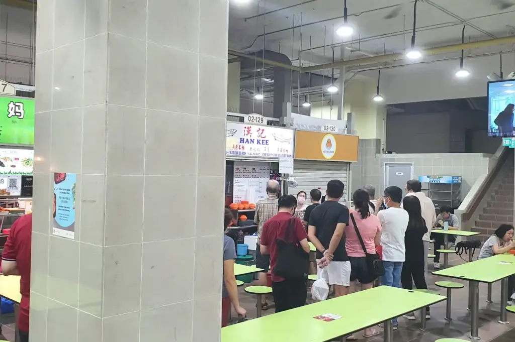 A small group of customers waiting in line at a closing food stall inside a Singapore hawker centre as surrounding stalls begin to shut down.