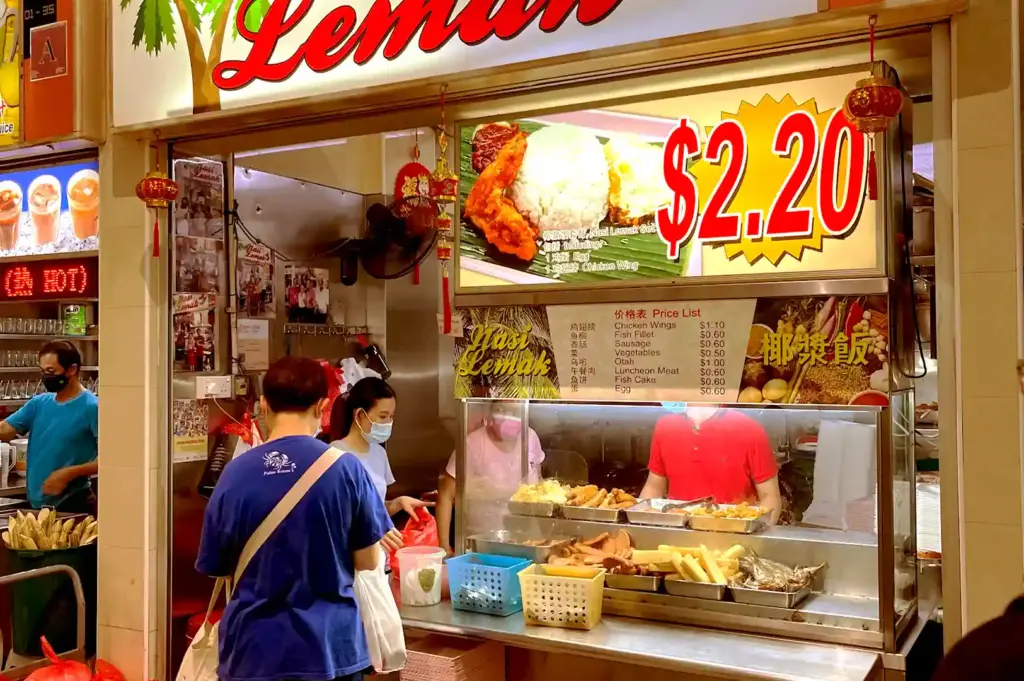 A hawker stall at Bedok Interchange Hawker Centre displaying a clear price list and a bright sign for a $2.20 Nasi Lemak set.