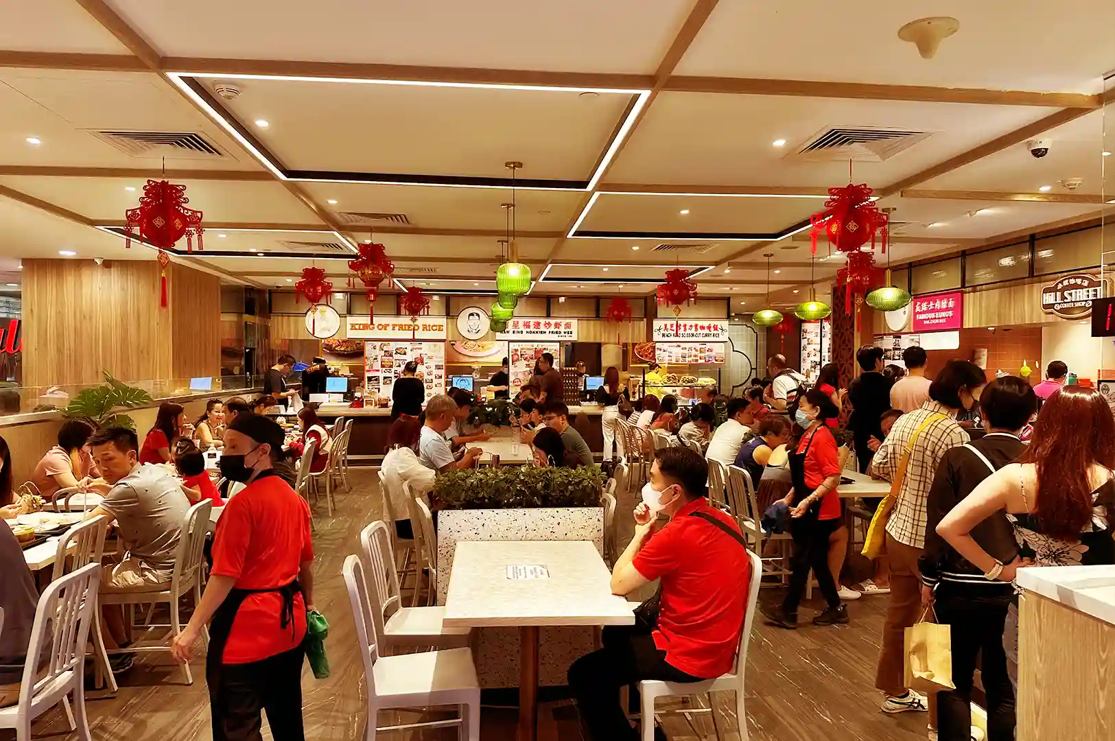 A bustling, brightly lit Singaporean hawker centre filled with diners, food stalls, and red festive lanterns, capturing a moment where unfamiliar sounds and movements dissolve into the comforting routine of everyday life.