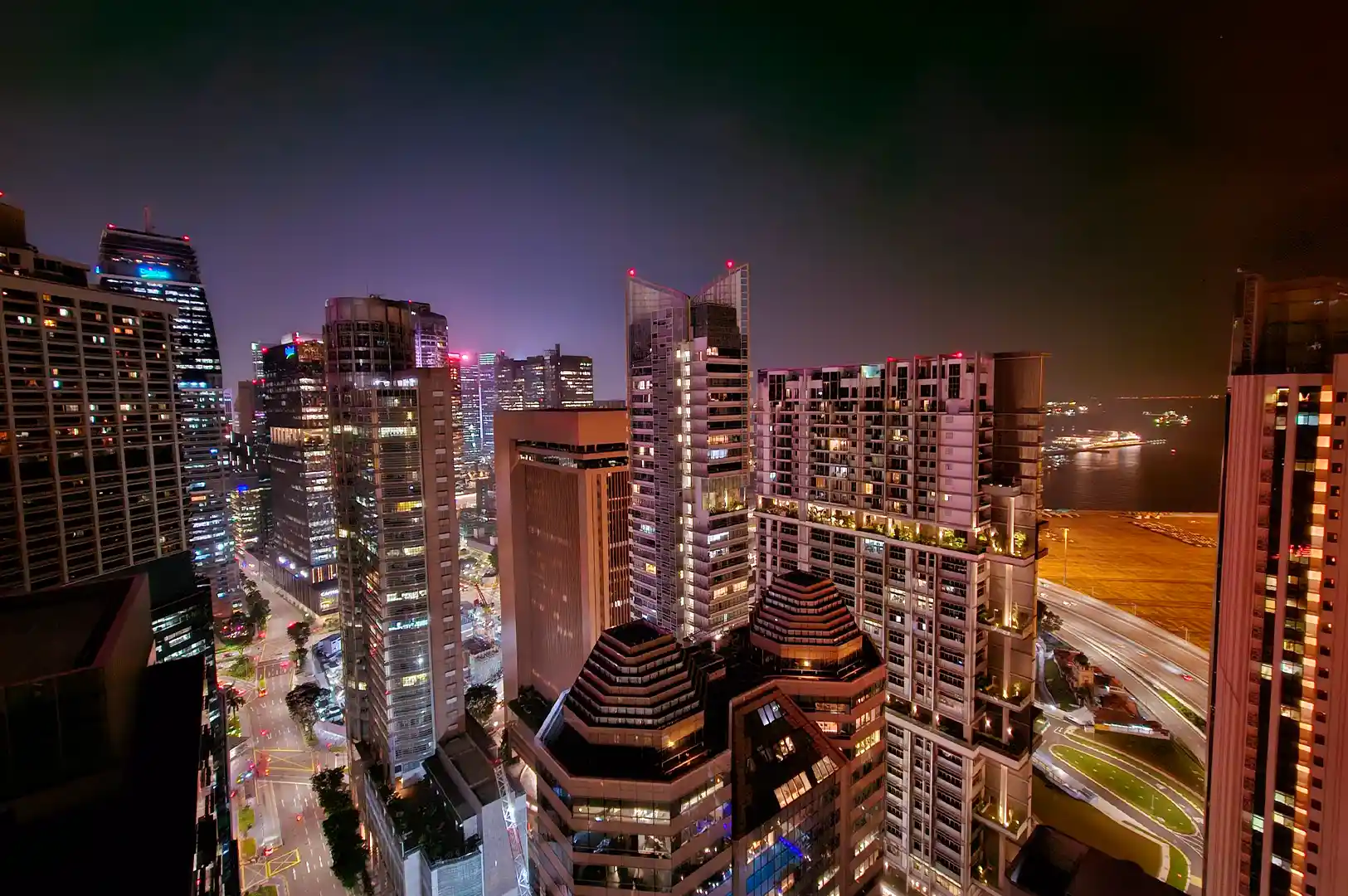 A scenic night view of illuminated skyscrapers and high-rise buildings across the Singapore skyline, capturing the city after dark.