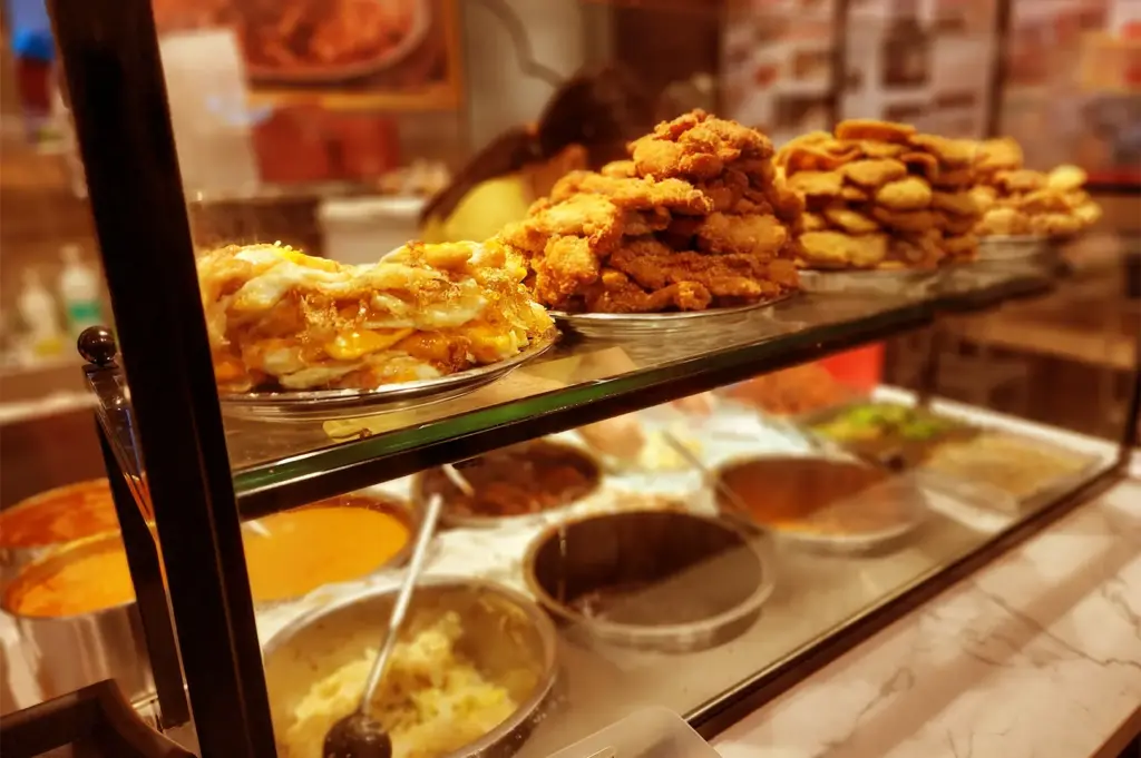 A hawker food stall display featuring stacked plates of golden-brown fried cutlets and rich curries, symbolizing the quiet warmth of familiarity replacing the need to keep searching.