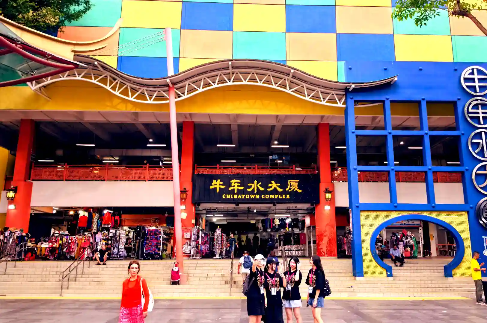 Exterior facade of Chinatown Complex in Singapore featuring colorful blue, yellow, and red checkerboard panels and a traditional Chinese roof design.