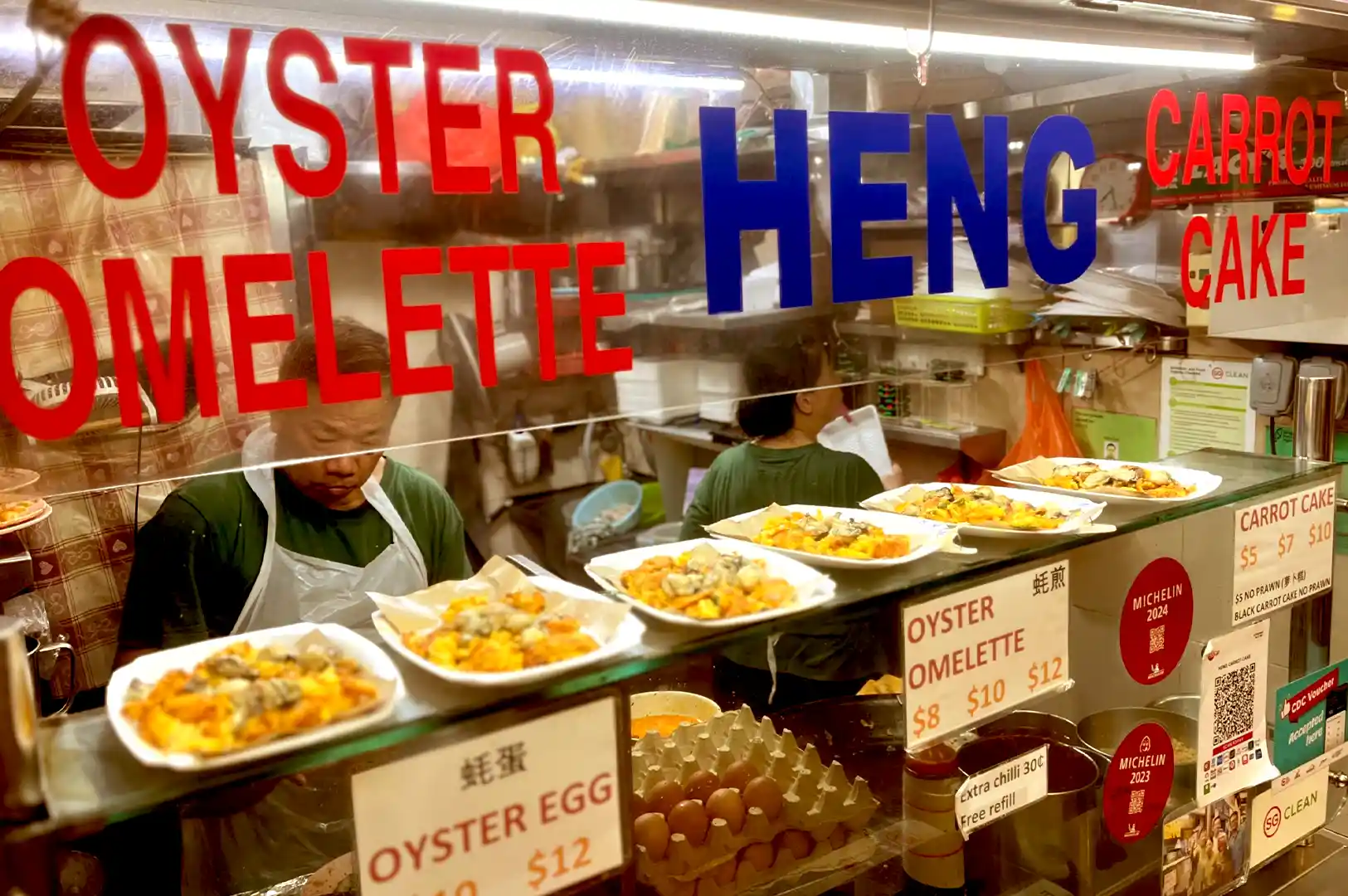 A hawker carefully preps fresh dishes behind a glass counter filled with plated oyster omelettes at Heng Carrot Cake & Oyster Omelette stall in Newton Food Centre.