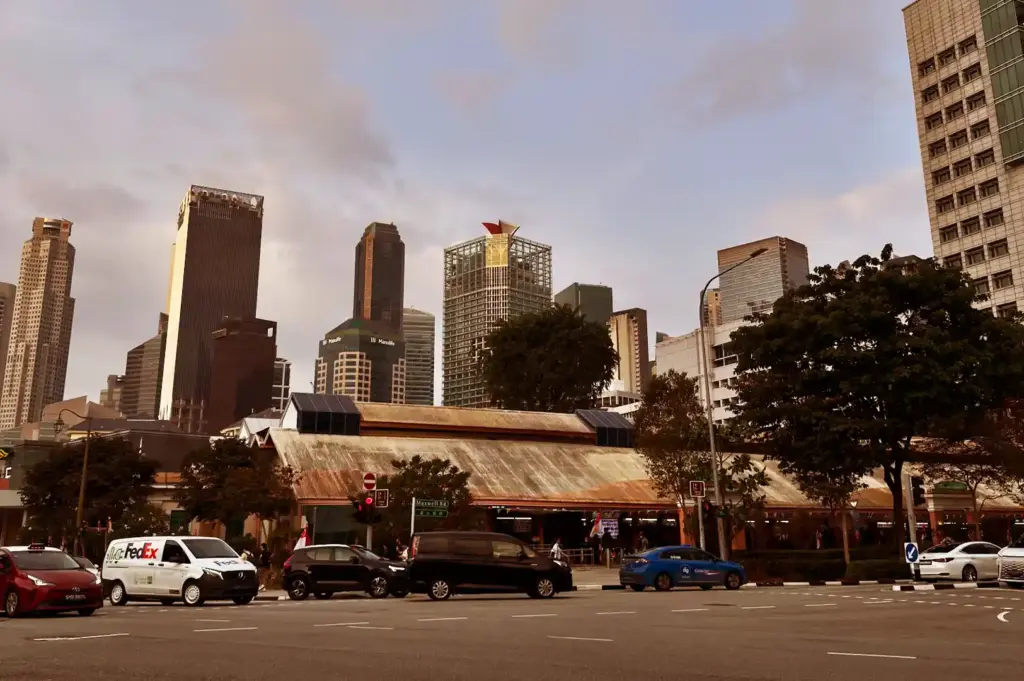 A wide view of Maxwell Food Centre's low-slung, rustic roofline juxtaposed against Singapore’s modern Central Business District skyline, tracing its evolution over time.