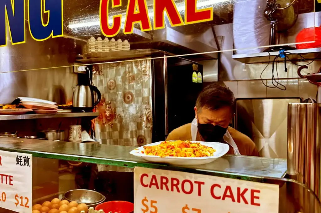 A freshly cooked plate of golden fried carrot cake resting on the glass serving shelf, ready to be lifted and served to waiting customers.