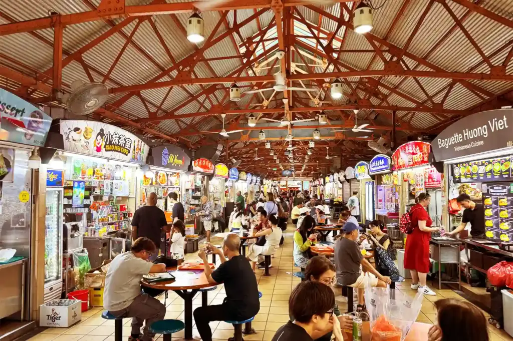 A bustling interior view of Maxwell Food Centre filled with vibrant food stalls and crowded tables, capturing the living heritage of everyday communal dining across generations.